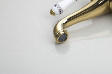 Nostalgische hoge goudkleurige wastafelkraan met witte elementen afgewerkt