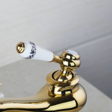 Nostalgische hoge goudkleurige wastafelkraan met witte elementen afgewerkt